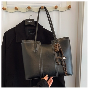 Detail of black tote bag featuring white contrast stitching and cute decorative charms
