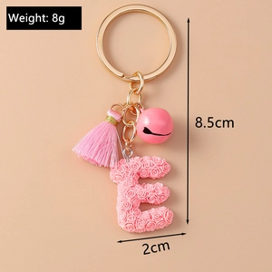 Macro shot of pink resin letter E keychain with rose pattern, tassel and bell charms