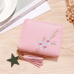 Pink PU leather short wallet with blue floral embroidery and tassel charm on wood surface