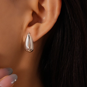 Gros plan d'une boucle d'oreille goutte d'argent avec finition miroir sur modèle