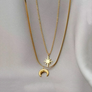 Double-layered gold necklace with star and moon pendants on elegant grey silk background