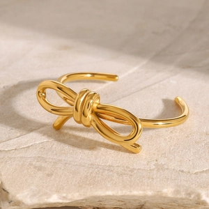 Detailed close-up of a golden bow-shaped open bangle on textured stone background