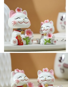 Close-up of white resin lucky cats with pink flowers and a red charm with Xi character