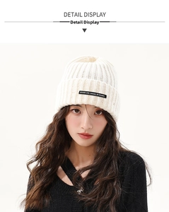 Detail view of cream chunky knit beanie with stylish black logo patch on the folded cuff