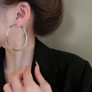 Detail view of large silver hoop earrings with sparkling texture worn by a model in black