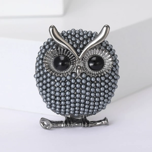 Macro shot of owl brooch with grey pearls and black gemstone eyes on a silver branch