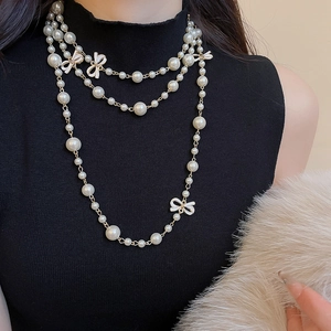 Detailed view of layered pearl necklace with white enamel bows on a black sweater