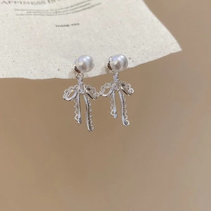 Macro view of silver bow pearl earrings with zircon detail on canvas display