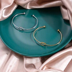 Close-up of minimalist gold and silver knot bangles displayed on silk fabric