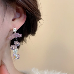 Detailed close-up of a purple heart flower earring with crystal beads on a model's ear
