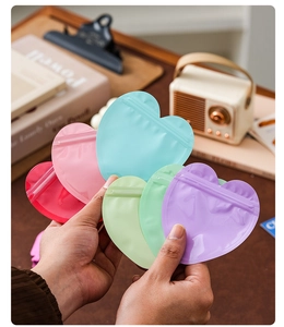Macro detail of heart-shaped macaron resealable bags in various colors held by hands