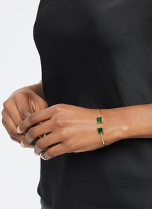 Close-up of a gold adjustable bracelet featuring two square green emerald stones