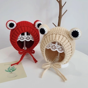 Detail view of red and beige knit frog hats with ear flaps and cute big eye decorations