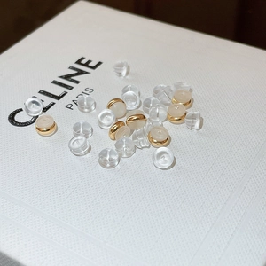 Mix of clear silicone and gold metal earring backs scattered on a white textured surface