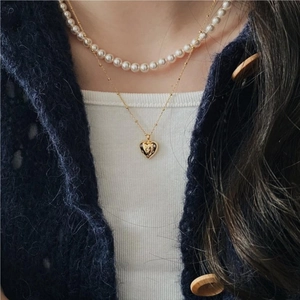 Close-up of a layered gold heart pendant and pearl necklace set on a blue cardigan