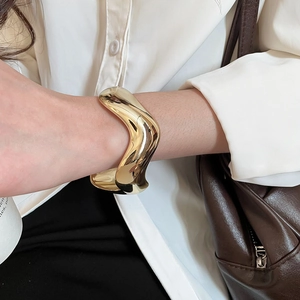 Gros plan d'un bracelet manchette doré ondulé porté avec une chemise blanche élégante