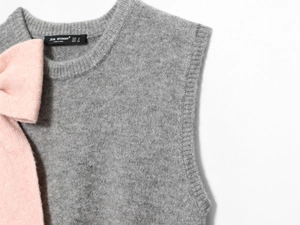 Dettaglio del gilet grigio in maglia con fiocco rosa felpato ed etichetta in raso nero