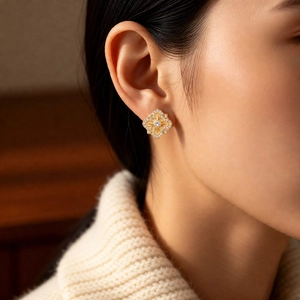 Detailed view of gold rhombic floral stud earrings with zircon on a model's ear