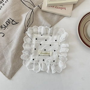 Close-up of white fabric coaster with black heart patterns and delicate lace edges