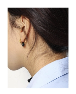 Close-up of gold knot earrings with black round charms worn by a model in a minimal style