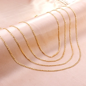 Macro view of five layered golden Figaro chain necklaces on champagne silk background