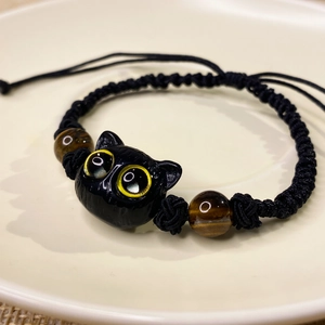 Macro shot of hand-woven black cord bracelet with a cute cat bead and tiger eye stones