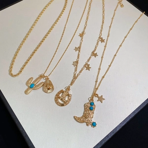 Detailed close-up of gold western cowboy hat, boot, and cactus pendants on layered chains