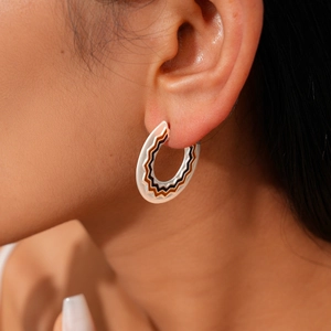 Detail view of silver C-shaped enamel earrings with black and brown wave patterns on ear