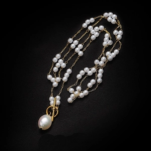 Multi-layer pearl necklace with large baroque pendant and gold toggle clasp on black surface