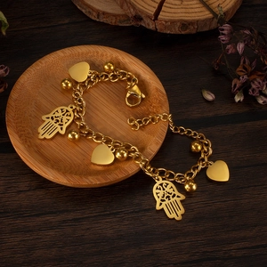 Detailed close-up of gold-tone heart and Hamsa hand charms on a chain bracelet
