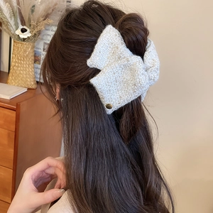 Detail of tweed bow hair claw with gold button accent and metallic silk threading