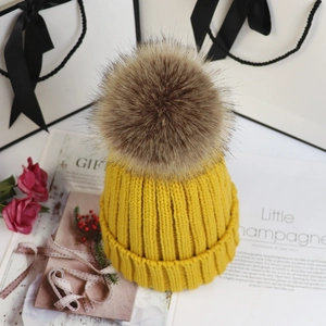 Detail der Strickstruktur einer gelben Wintermütze mit großem braunem Kunstpelz-Bommel