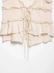 Close-up of cream knitted camisole top featuring tiered ruffles and delicate front tie strings