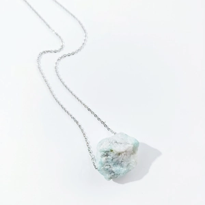 Close-up of irregular light blue natural raw crystal pendant with silver link chain