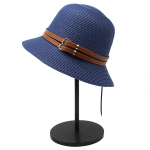Navy blue straw sun hat with brown leather straps and gold buckles on a display stand