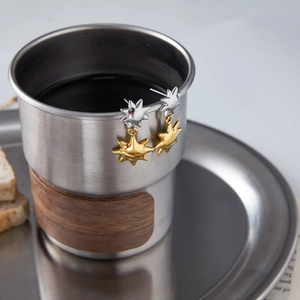 Two-tone sunburst stainless steel earrings hanging on a metal cup in a lifestyle setting