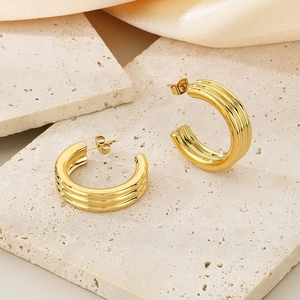 Detail of gold C-shaped earrings with triple groove texture on stone and satin
