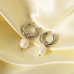 Close-up detail of stainless steel hoop earrings with natural pearl pendants on silk.
