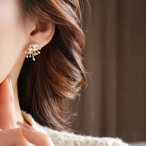 Close-up of elegant gold flower earrings with pearls and crystals worn by a model