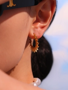 Macro shot of 18K gold plated C-shaped earrings featuring a radiant sunburst spiked design