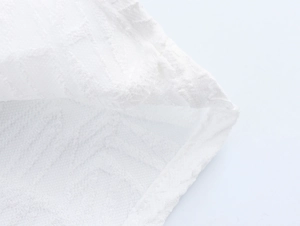 Macro shot of white textured jacquard fabric with elegant wave patterns and neat hem stitching