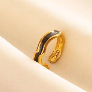 Dettaglio macro dell'anello dorato con smalto nero su morbido tessuto beige pieghettato