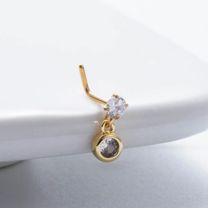 Détail d'un piercing de nez en forme de L doré avec oxydes de zirconium et pendentif