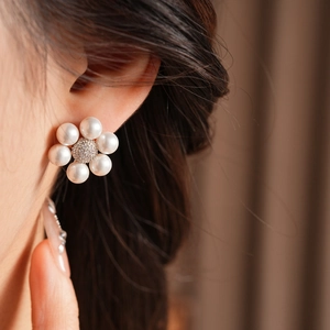 Close-up of flower-shaped earrings with white pearls and sparkling zircon on a model