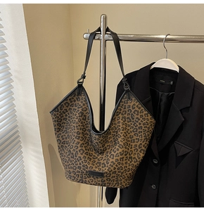 Detail of leopard print tote bag with black straps and brand patch on neutral background