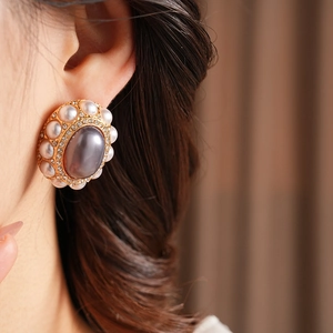 Close-up of vintage gold earrings with purple zircon and pearls on a model ear
