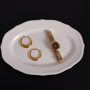 Flat lay of chunky gold moon earrings and vintage gold watch on a white ceramic tray