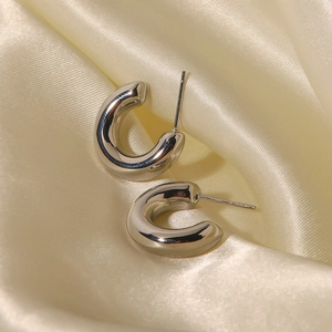 Close-up of polished silver C-shaped earrings resting on a smooth beige silk fabric