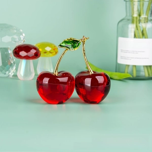 Detail of red crystal cherry ornament with golden stem and green leaf on desk
