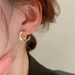 Close-up of golden crescent moon earrings with crystal charm worn by a model